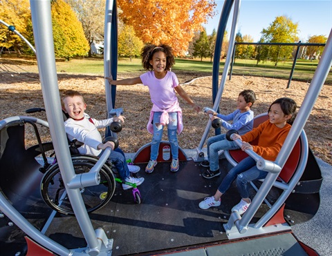 three kids swinging on a We-Go-Swing - the boy on the left is in a wheelchair